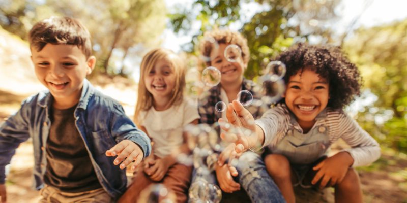 Group of children playing with soap bubbles outdoors. Friends trying to catch the bubbles.