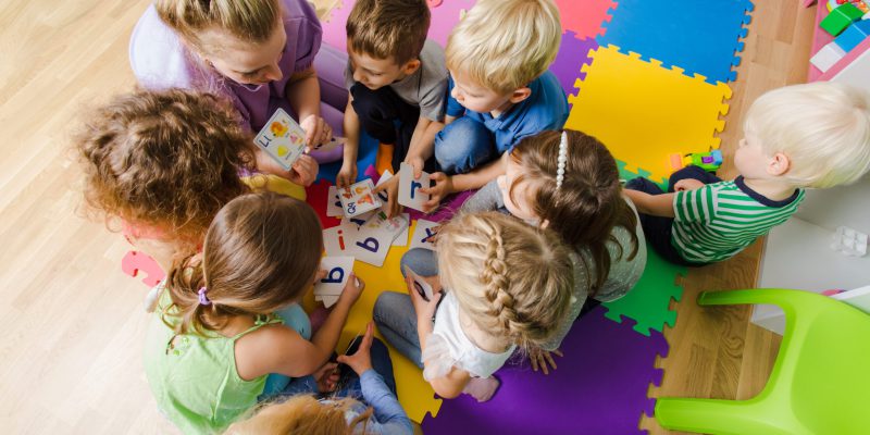 Group of kindergarten kids sitting closely on a floor together with teacher, providing group work. Children learning to cooperate while solving tasks.